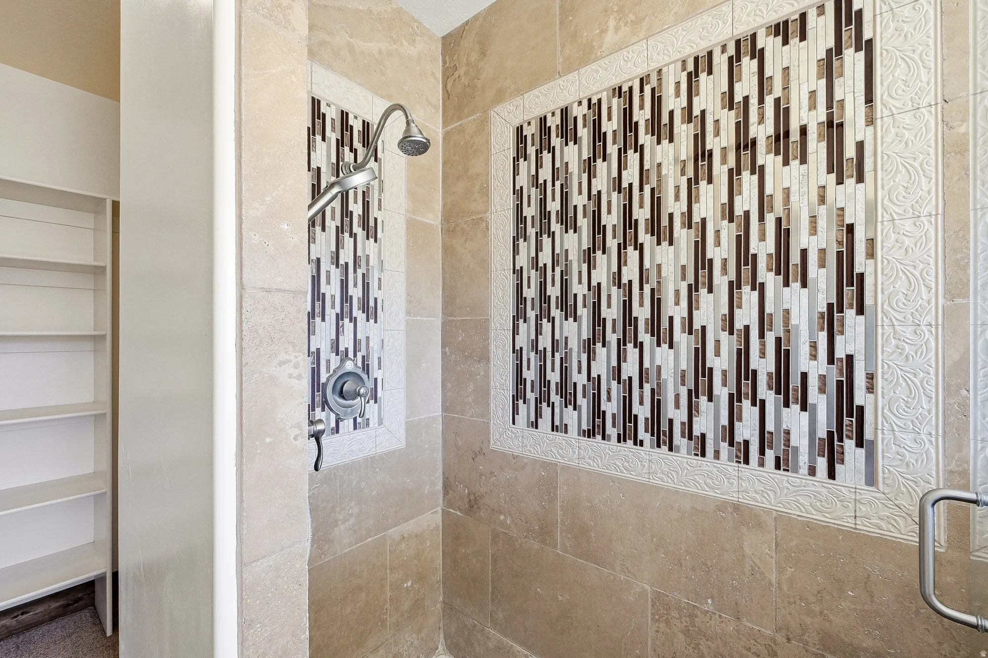 Shower featuring natural stone tile walls and a mosaic tile accent panel with decorative trim