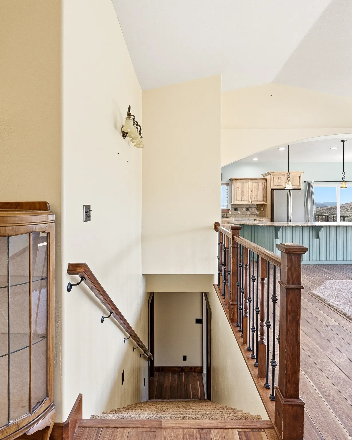 Wood-finish flooring with a staircase featuring a dark wood handrail and black iron balusters