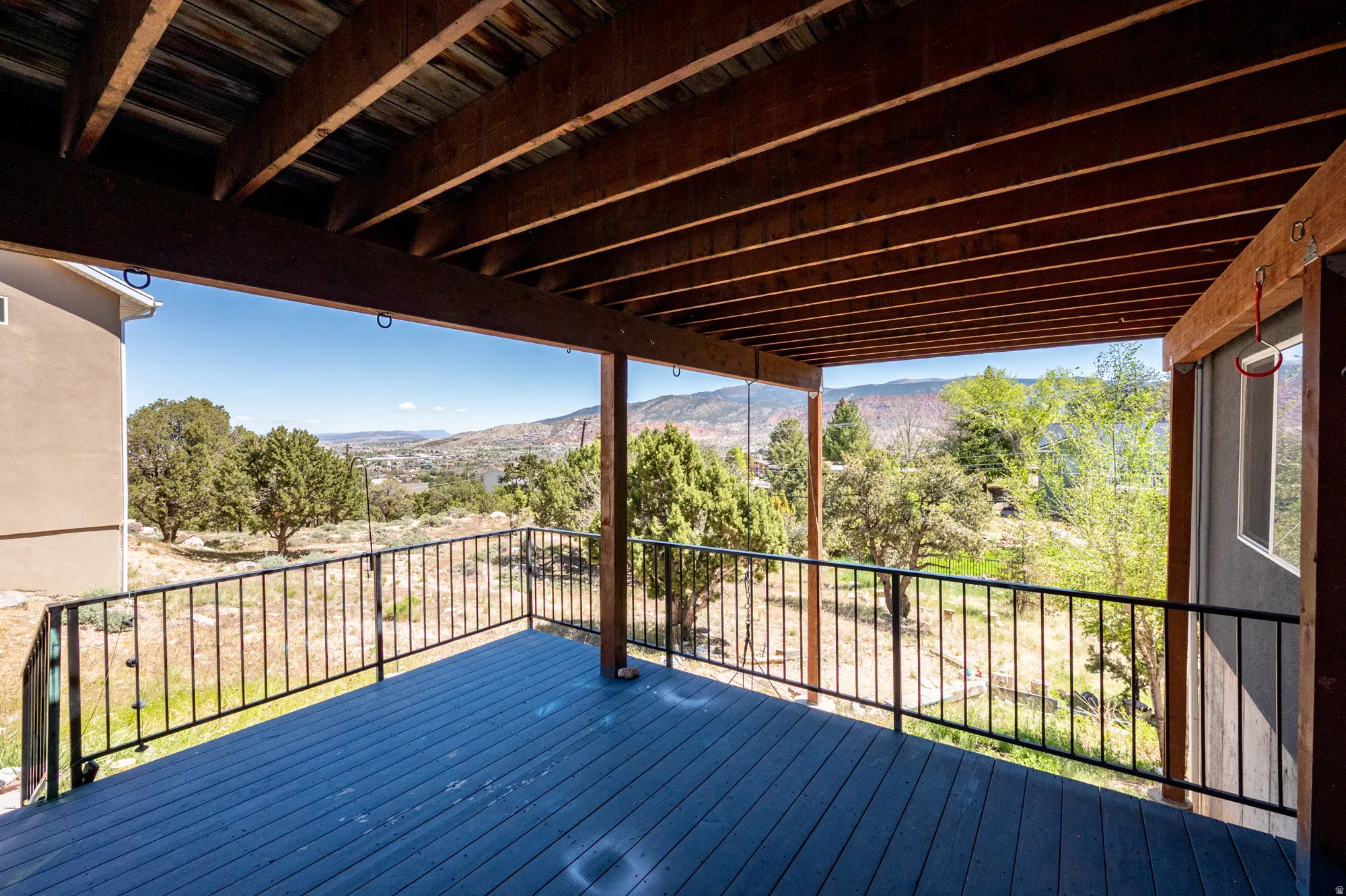 Covered deck featuring a composite surface, dark wood beam ceiling, black metal railings, and a distant mountain landscape