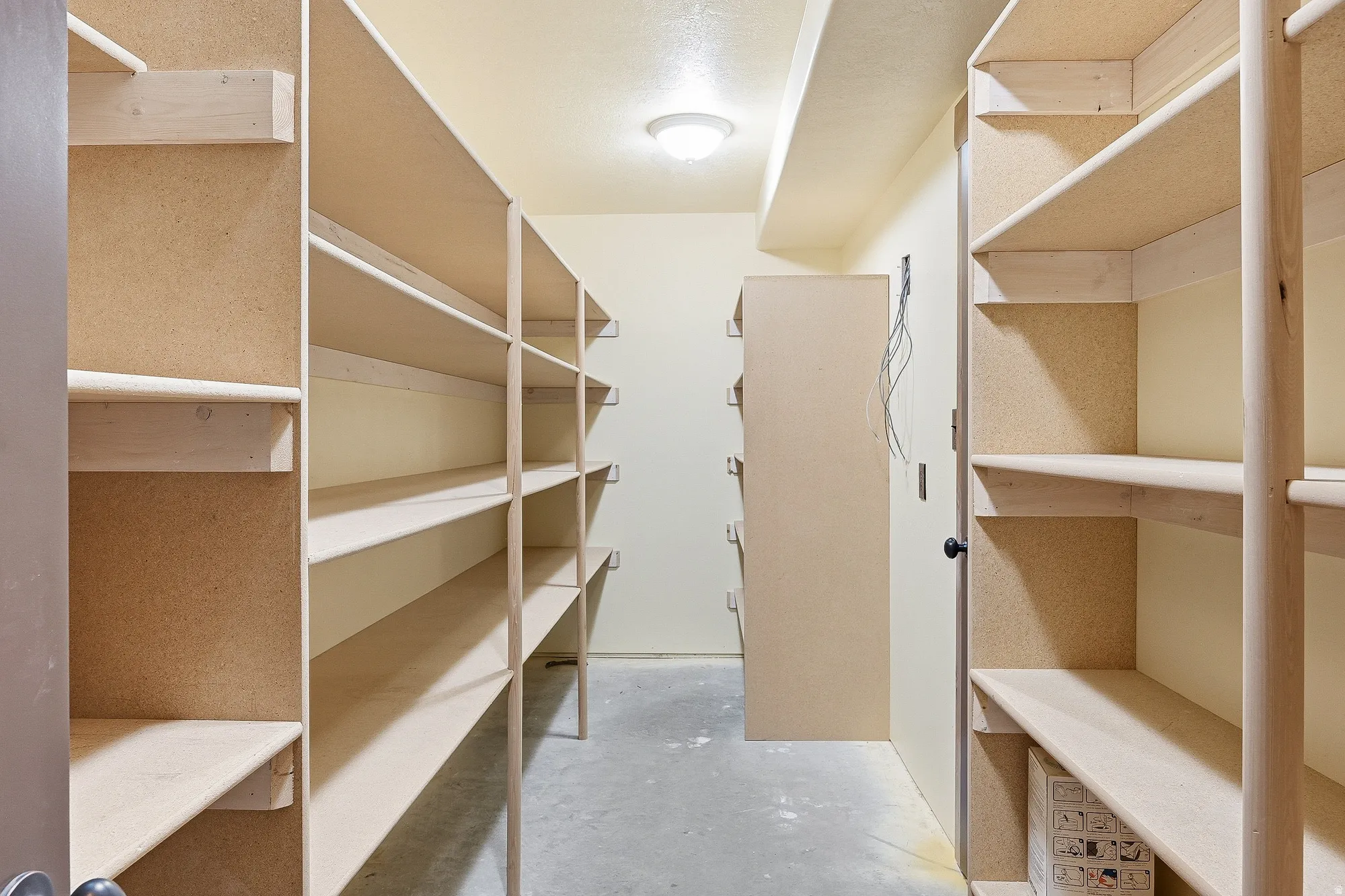 Dedicated storage room featuring extensive built-in shelving, durable light-colored walls, overhead lighting, and a concrete floor