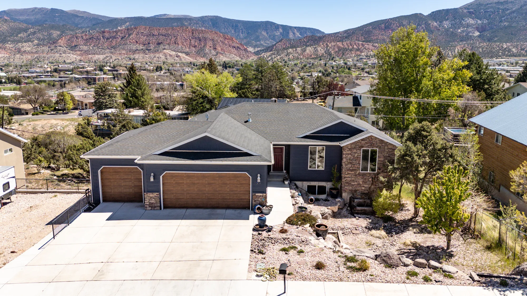 Contemporary home featuring a dark blue facade with stone accents, a two-car garage with wood-finish doors, a concrete driveway, and a front pathway