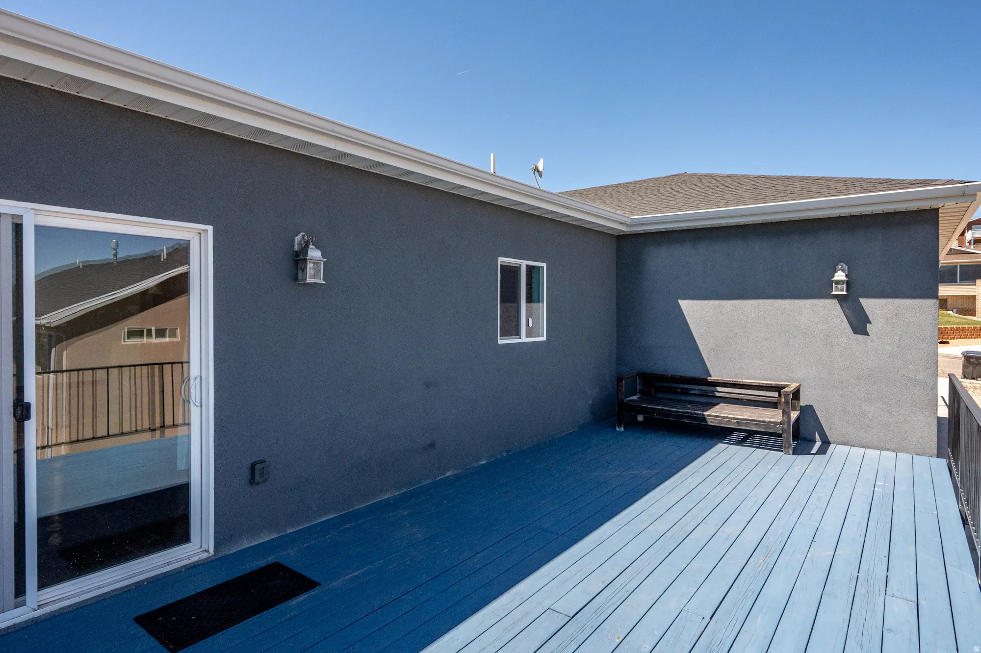 Exterior deck featuring a blue-painted surface, gray stucco siding, white window trim, and a sliding glass door