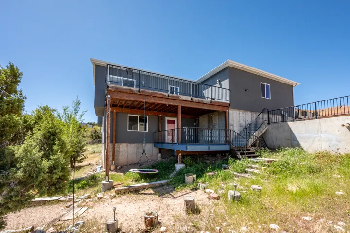 Two-story exterior with a gray facade, featuring an upper-level deck with black railings and a lower-level covered patio with wood supports