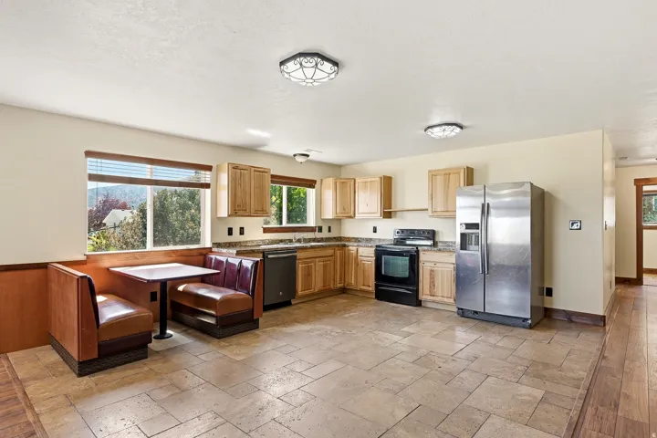 Spacious kitchen with a built-in booth seating area, light wood cabinetry, stone-look countertops, and stainless steel appliances