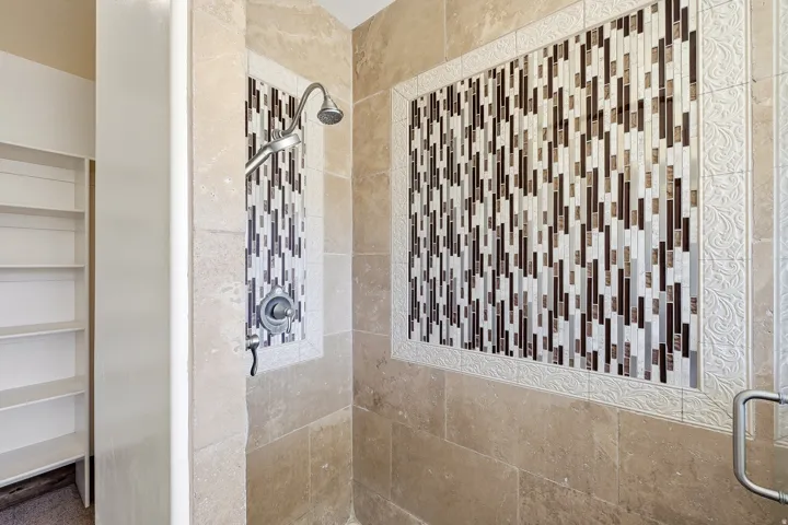 Shower featuring natural stone tile walls and a mosaic tile accent panel with decorative trim