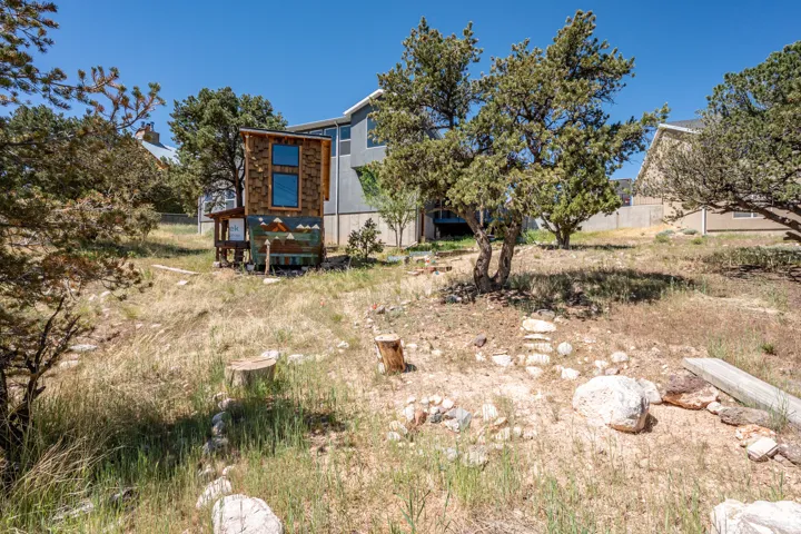 Wood-sided outbuilding with vertical windows, situated on a sloped, natural landscape featuring mature trees and scattered boulders