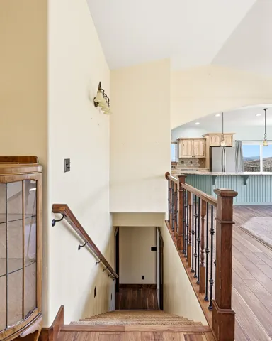 Wood-finish flooring with a staircase featuring a dark wood handrail and black iron balusters