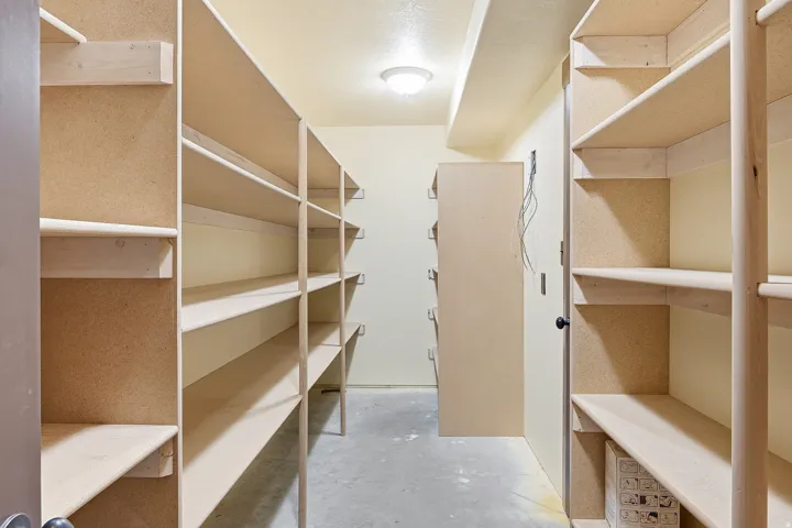 Dedicated storage room featuring extensive built-in shelving, durable light-colored walls, overhead lighting, and a concrete floor