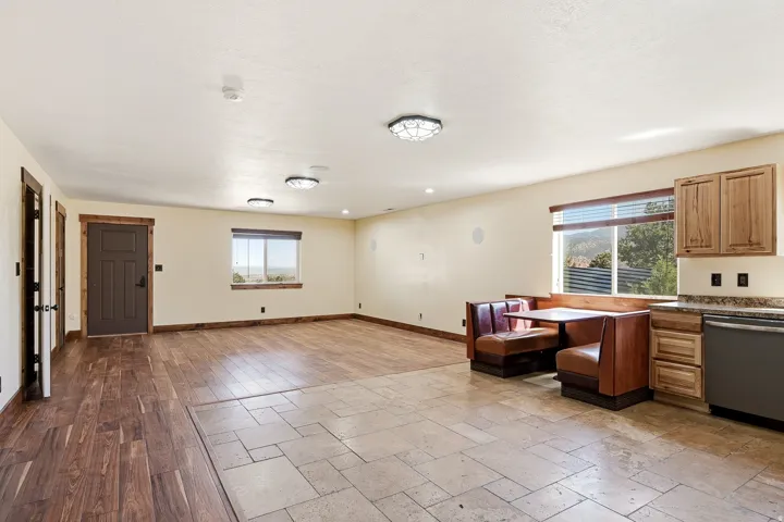 Open-concept living space featuring distinct wood-finish flooring and tile flooring, a kitchen area with wood cabinetry and stone countertops, and a built-in dining booth
