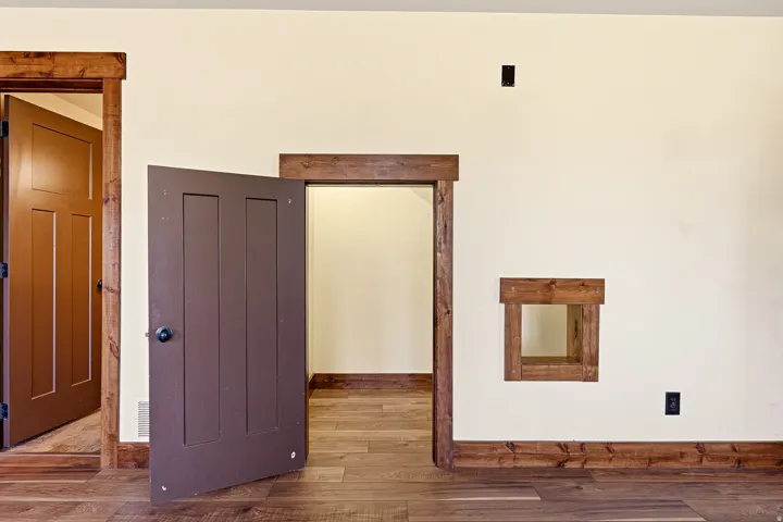 Panel doors with dark hardware, natural wood-finish trim, coordinating wood-finish baseboards, and wood-finish flooring