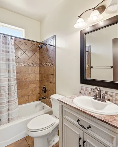 Bathroom featuring a white bathtub, a tiled shower surround with decorative accent band, and a single vanity with a white countertop basin and bronze-finish faucet