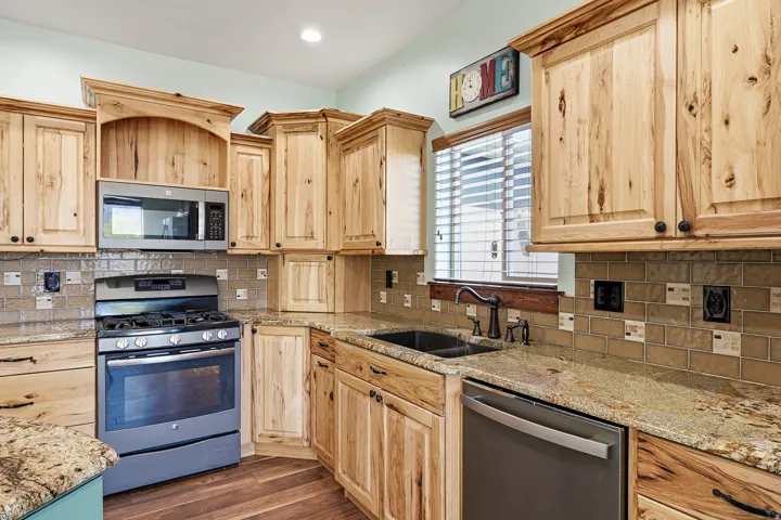 Kitchen featuring natural wood cabinetry, granite countertops, tile backsplash, wood-finish flooring, and stainless steel appliances