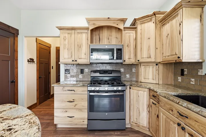 Kitchen featuring light wood cabinetry, stone countertops, a tile backsplash, and stainless-steel appliances including a range and microwave
