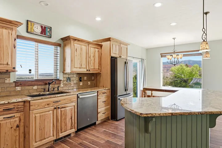 Kitchen featuring natural wood cabinetry, light-toned granite countertops, stainless steel appliances, and wood-finish flooring