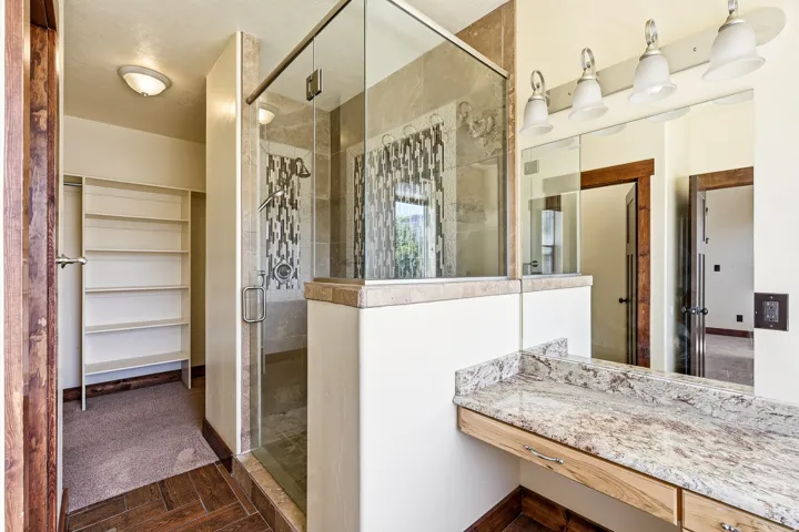 Glass-enclosed shower with decorative tile accent wall, granite countertop vanity, built-in shelving, and wood-finish flooring