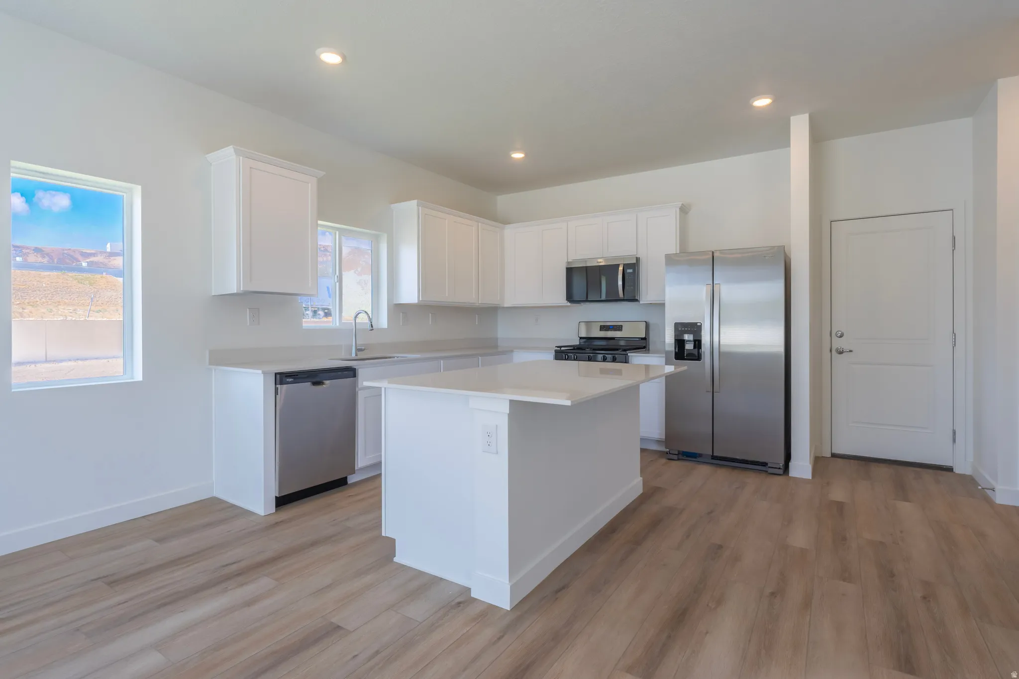Kitchen featuring white cabinetry, light-toned countertops, a central island, stainless steel appliances, and wood-finish flooring