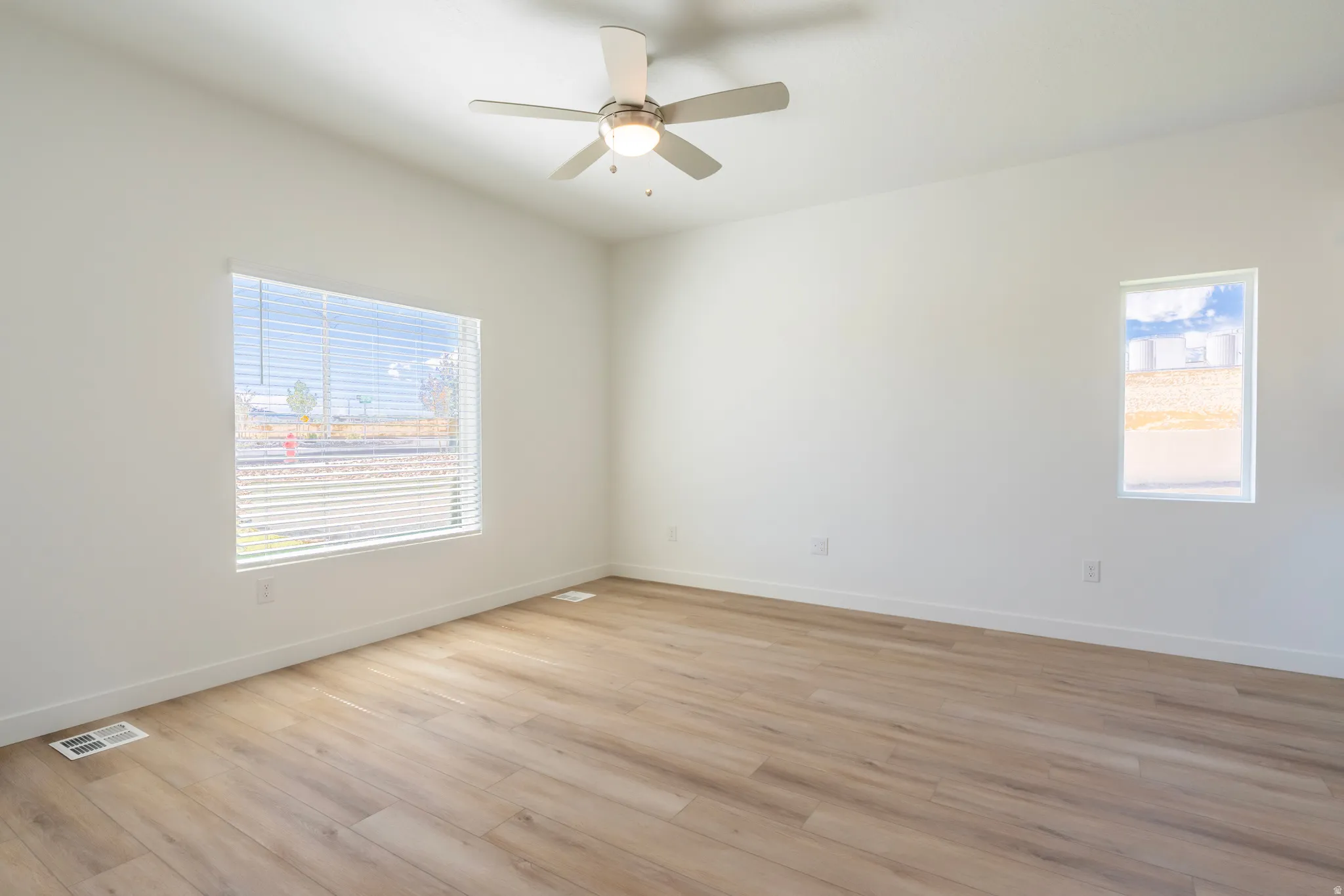 Neutral wall paint, wood-finish flooring, ceiling fan with integrated lighting, and multiple windows