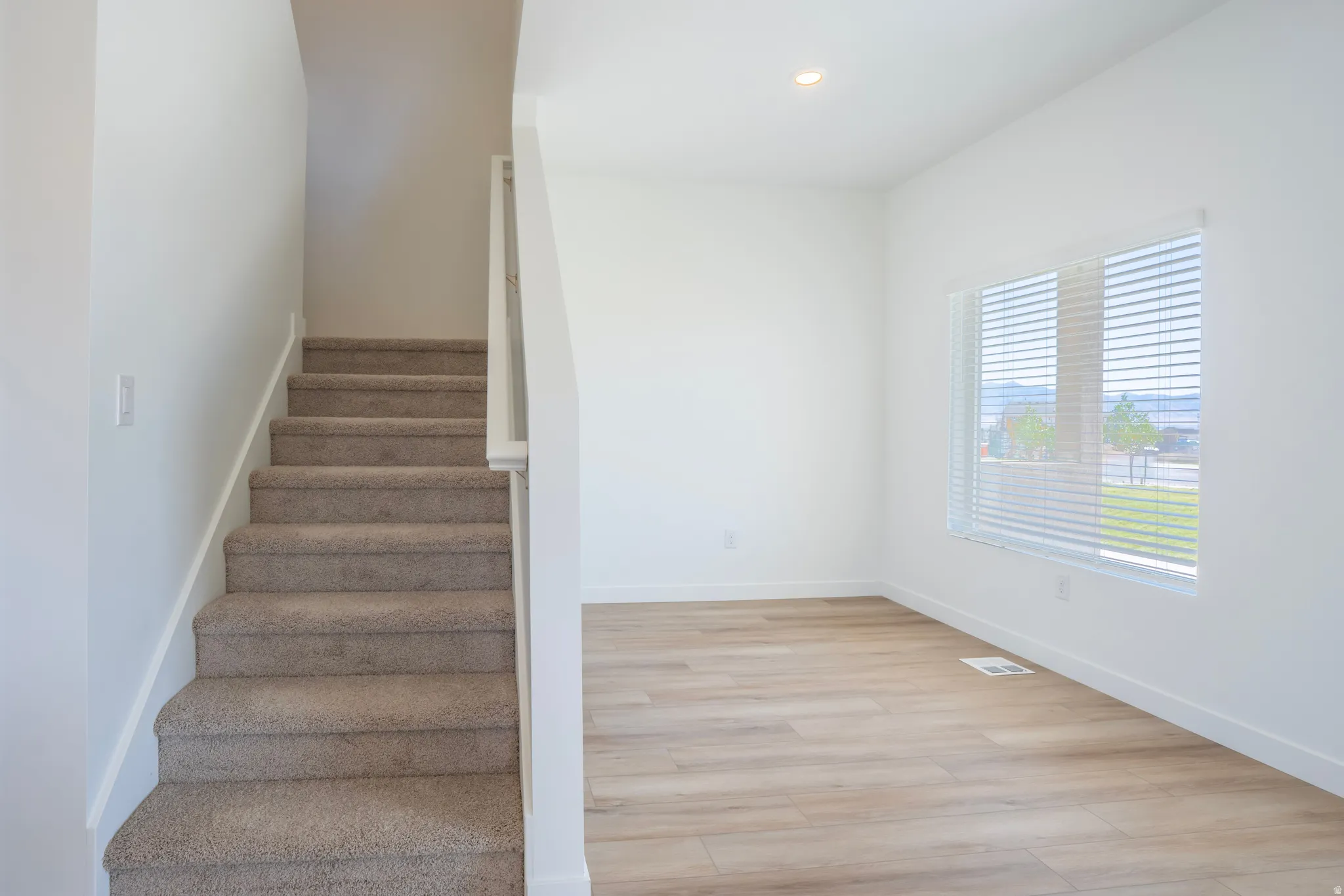 Carpeted staircase, wood-finish flooring, recessed lighting, and large windows with blinds