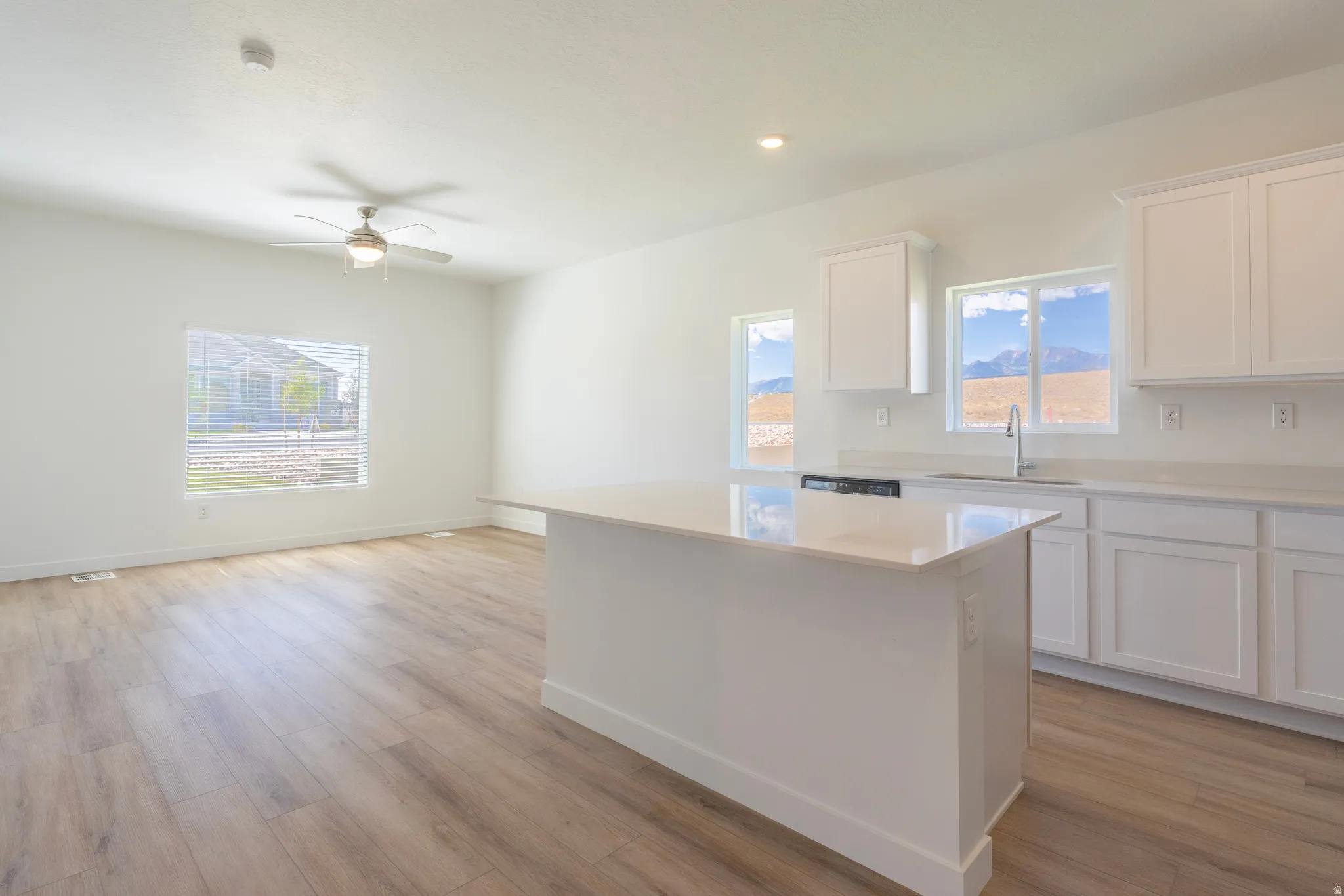 Contemporary kitchen featuring white cabinetry, light-toned countertops, a central island, and wood-finish flooring