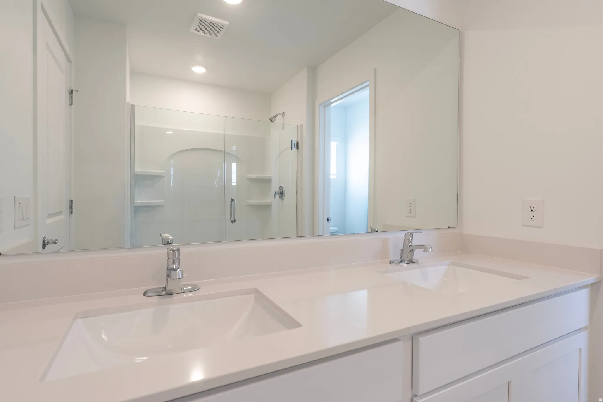Dual undermount sinks with chrome faucets, light-toned countertop, white cabinetry, and a large wall mirror