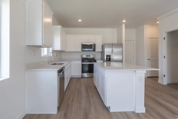 Kitchen featuring white cabinetry, light-toned countertops, stainless steel appliances, a center island with a breakfast bar, and wood-finish flooring