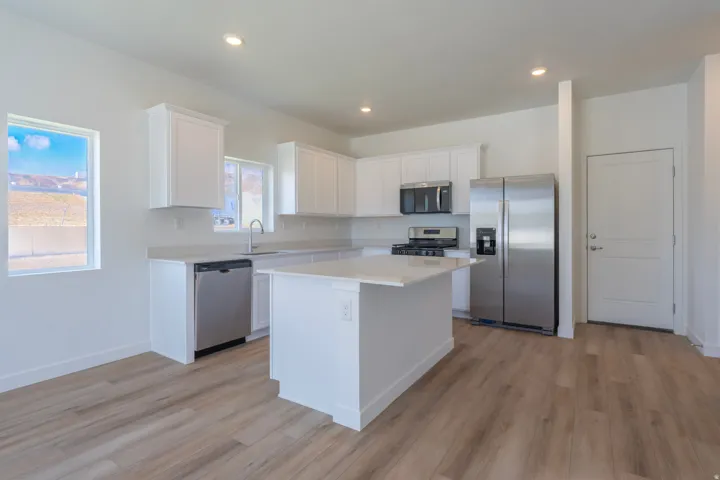 Kitchen featuring white cabinetry, light-toned countertops, a central island, stainless steel appliances, and wood-finish flooring