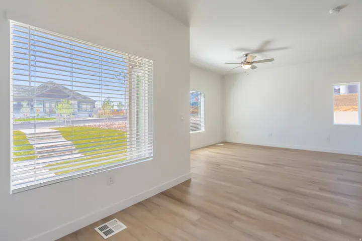 Expansive room with wood-finish flooring, white walls, and a ceiling fan with integrated lighting