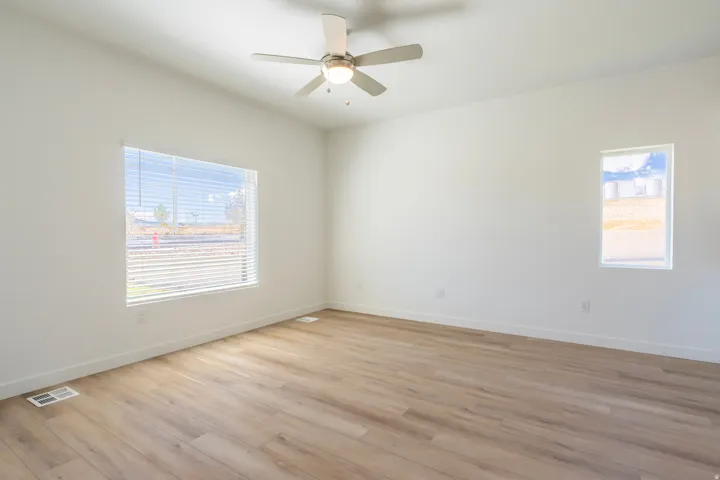 Neutral wall paint, wood-finish flooring, ceiling fan with integrated lighting, and multiple windows
