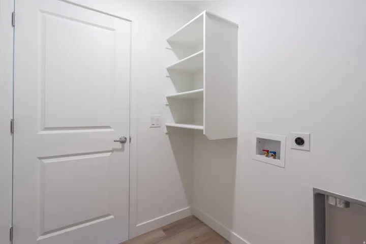 White paneled door with brushed nickel hardware, built-in white shelving, wood-finish flooring, and laundry hookups