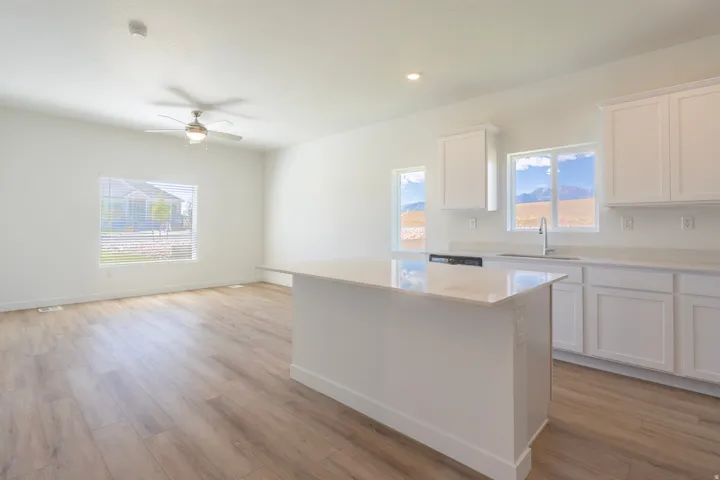 Contemporary kitchen featuring white cabinetry, light-toned countertops, a central island, and wood-finish flooring