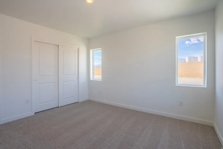Bright secondary bedroom showcasing neutral wall finishes, carpet flooring, dual closets with panel doors, and abundant natural light from a large window framing outdoor scenery