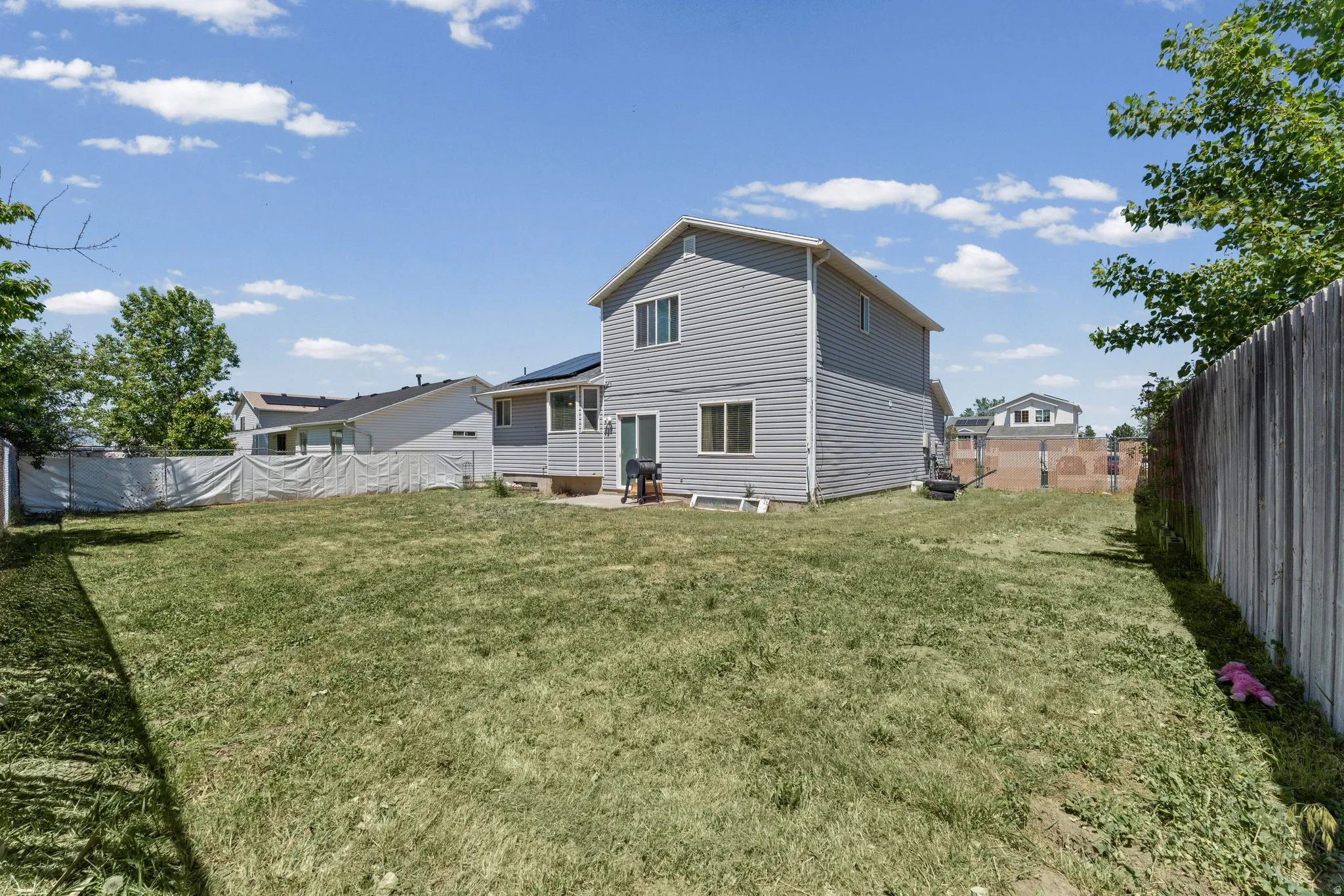 Spacious backyard featuring a large green lawn, a privacy fence, and a concrete patio