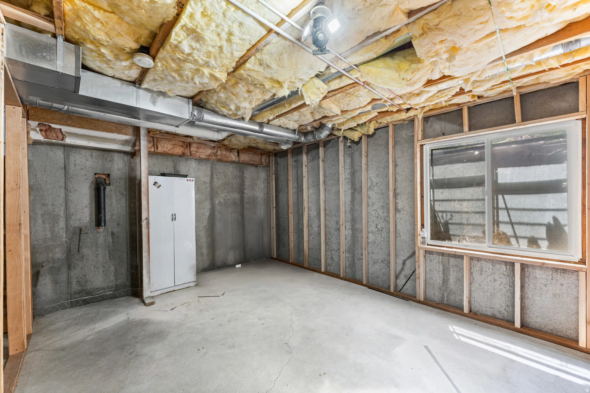 Unfinished basement with concrete walls, exposed ceiling insulation, and a sliding window
