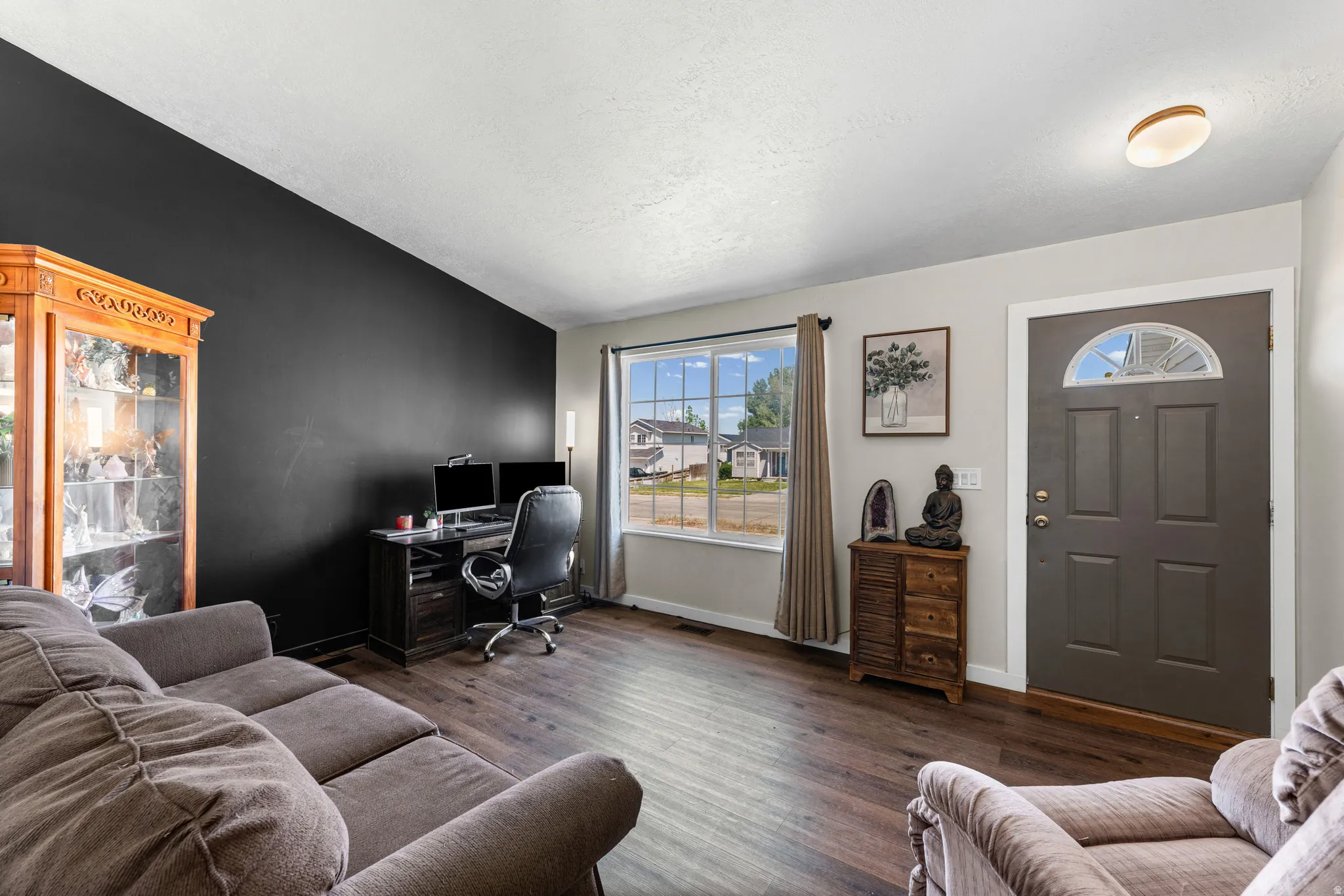 Spacious living area featuring wood-finish flooring, a prominent accent wall, and ample natural light through a large picture window