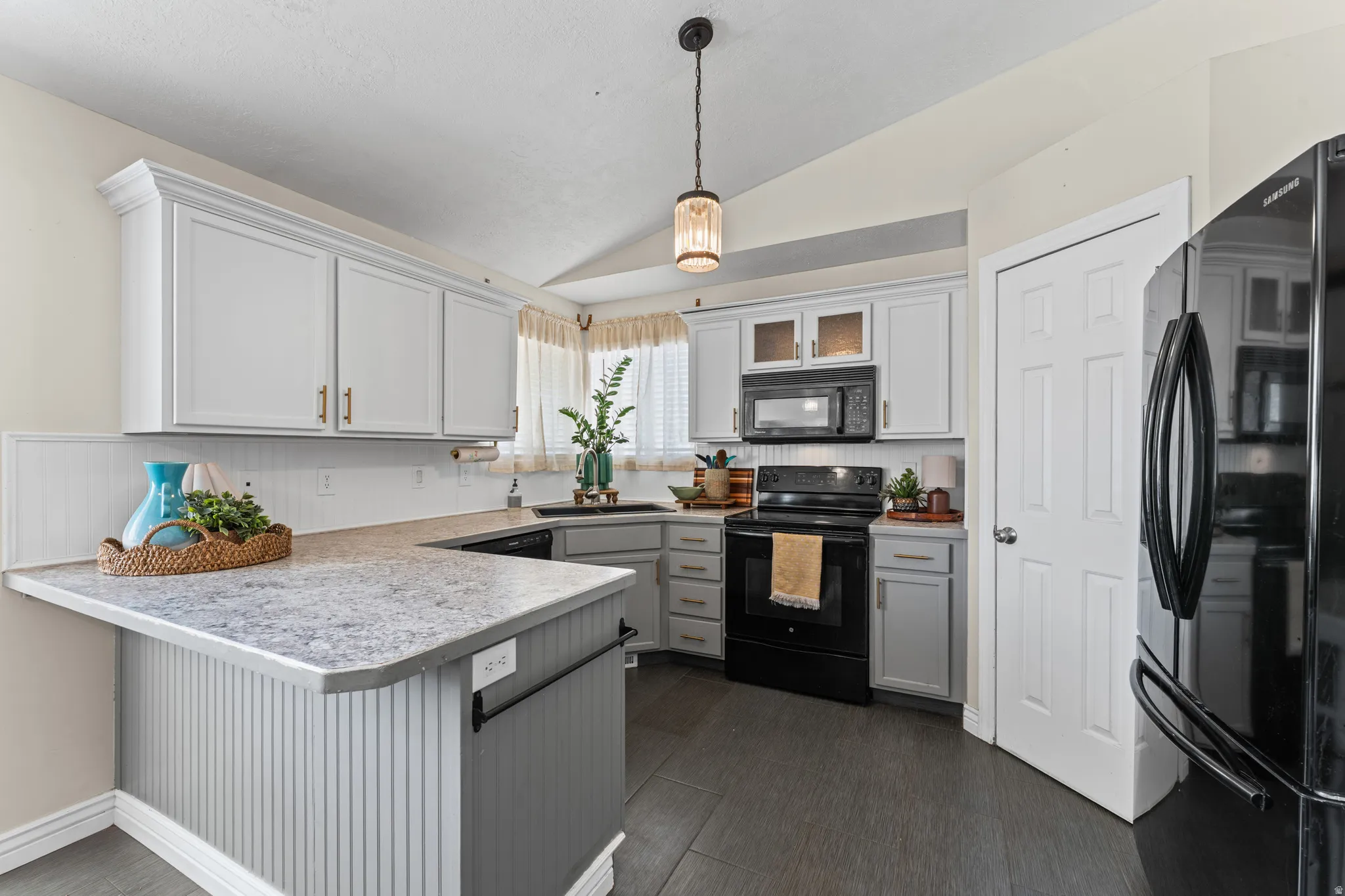 Kitchen featuring white upper cabinetry with gold-tone hardware, grey lower cabinetry, and a white beadboard backsplash