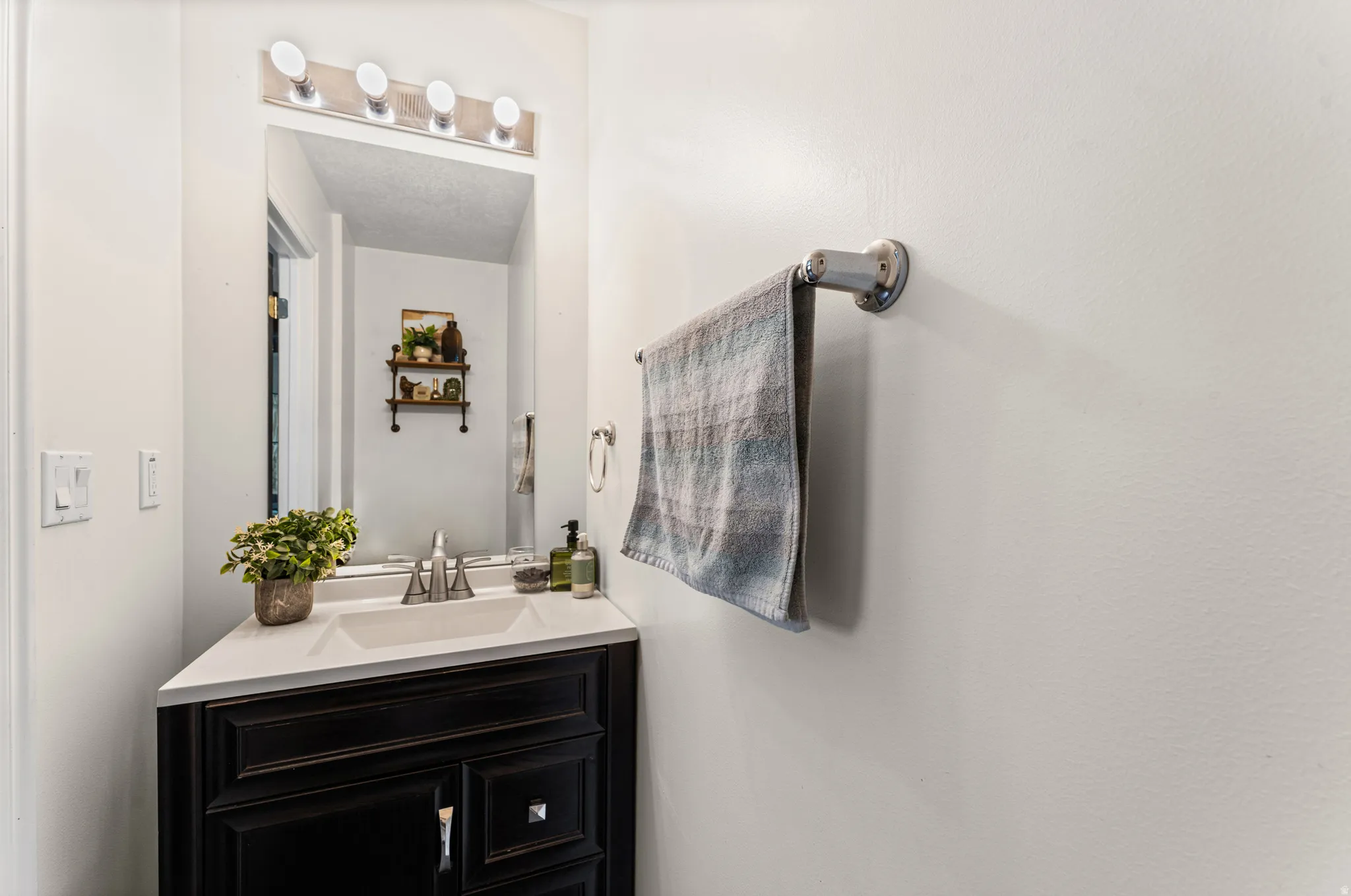 Bathroom vanity featuring a dark wood-finish cabinet with silver hardware, a white countertop, and an undermount sink