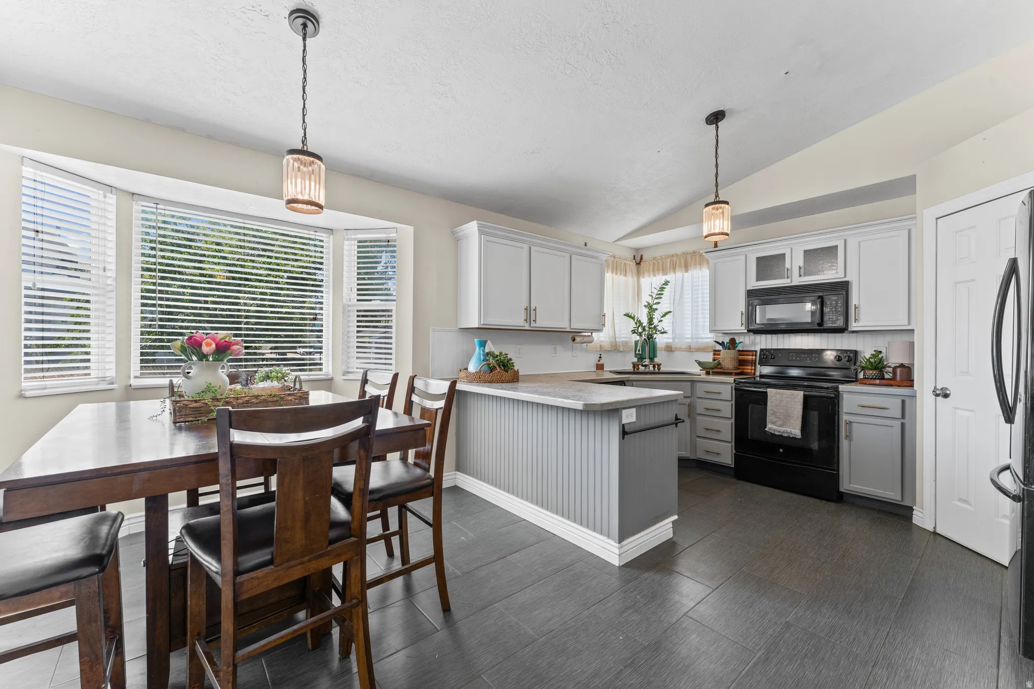 Kitchen and dining area featuring dark tile flooring, a bay window, light gray cabinetry, and black appliances