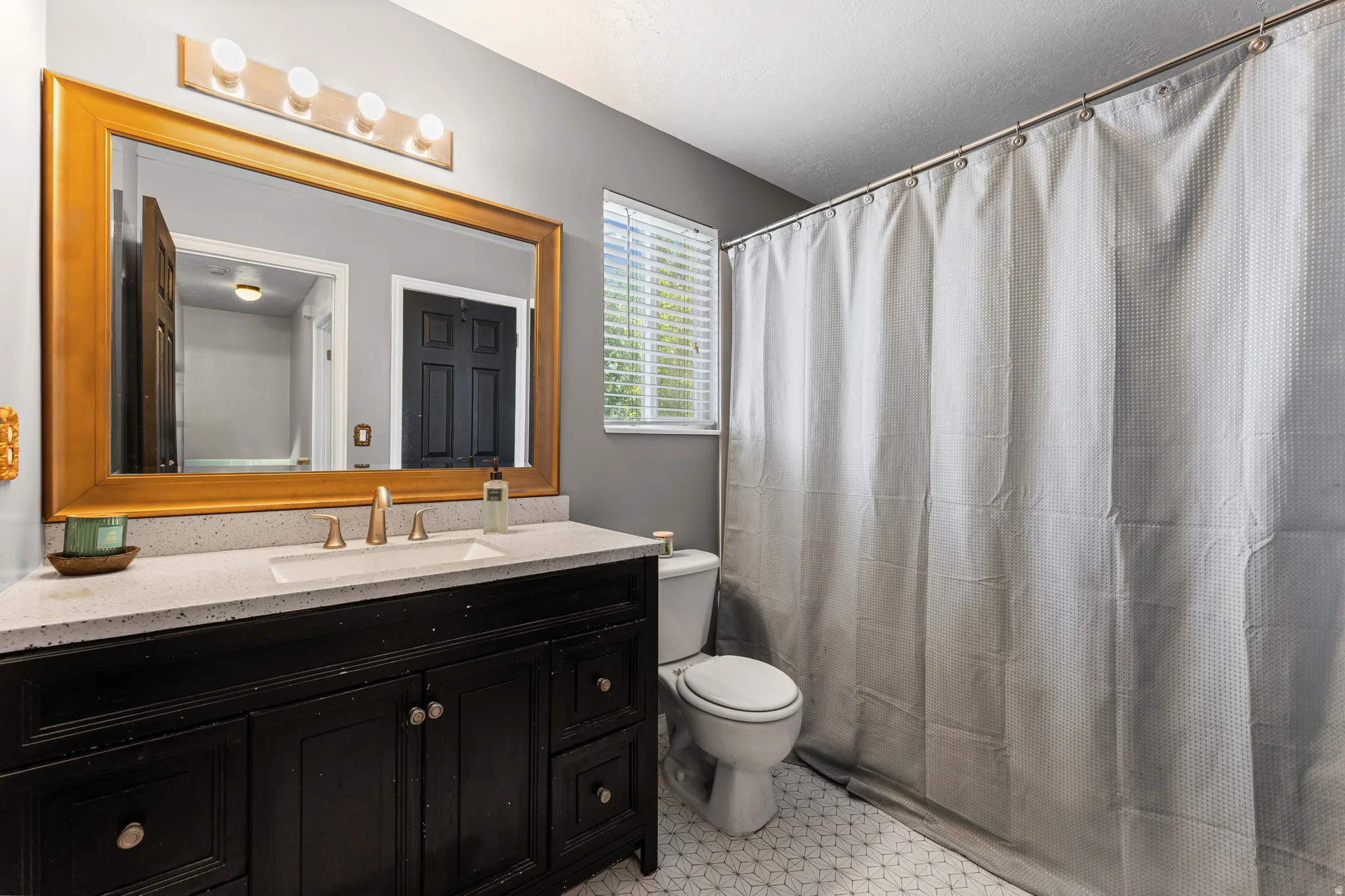 Bathroom featuring a dark wood vanity with a light-toned countertop, a large framed mirror, and a wall-mounted light fixture