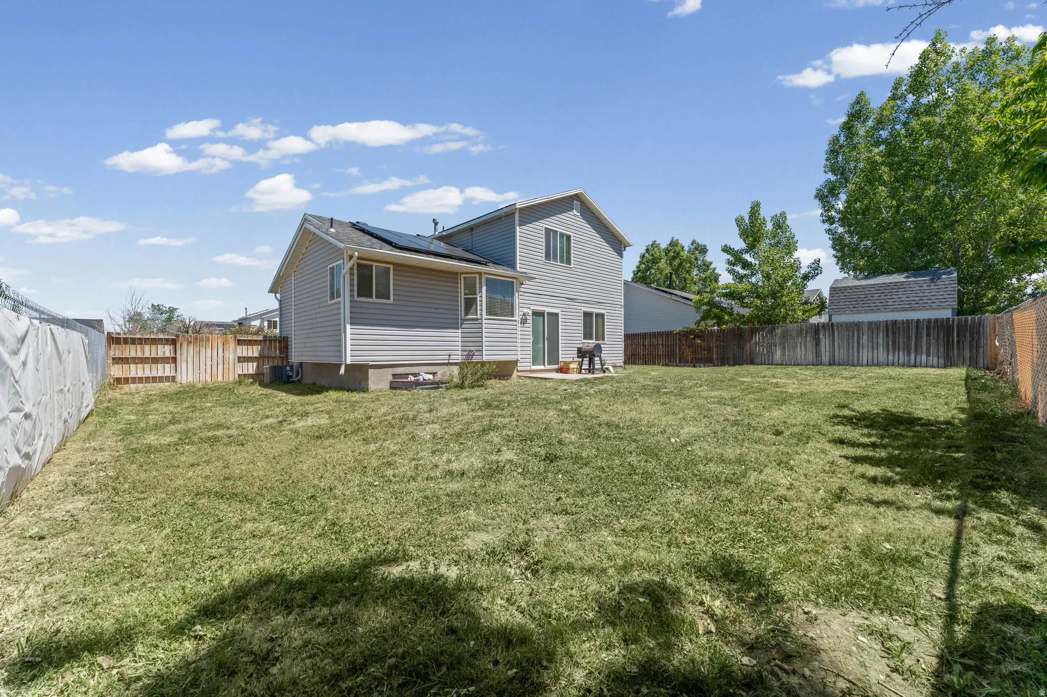 Expansive rear yard featuring a large grass area, wood fencing, and a concrete patio