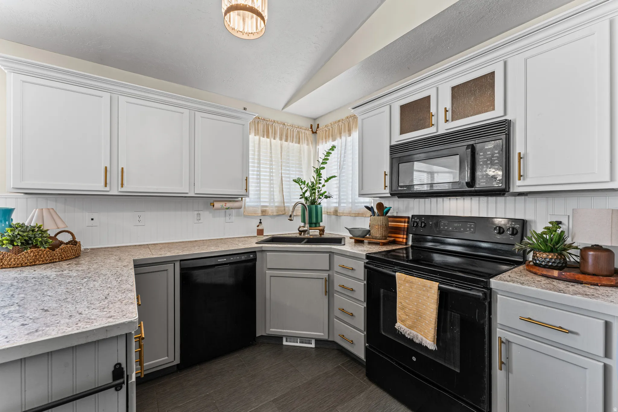 Kitchen featuring white upper cabinetry with gold-tone hardware, grey lower cabinetry, a black appliance package, and light-toned countertops