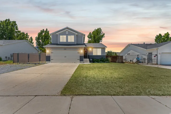 Two-story residence featuring a two-car garage with overhead lighting, a concrete driveway, and a front lawn