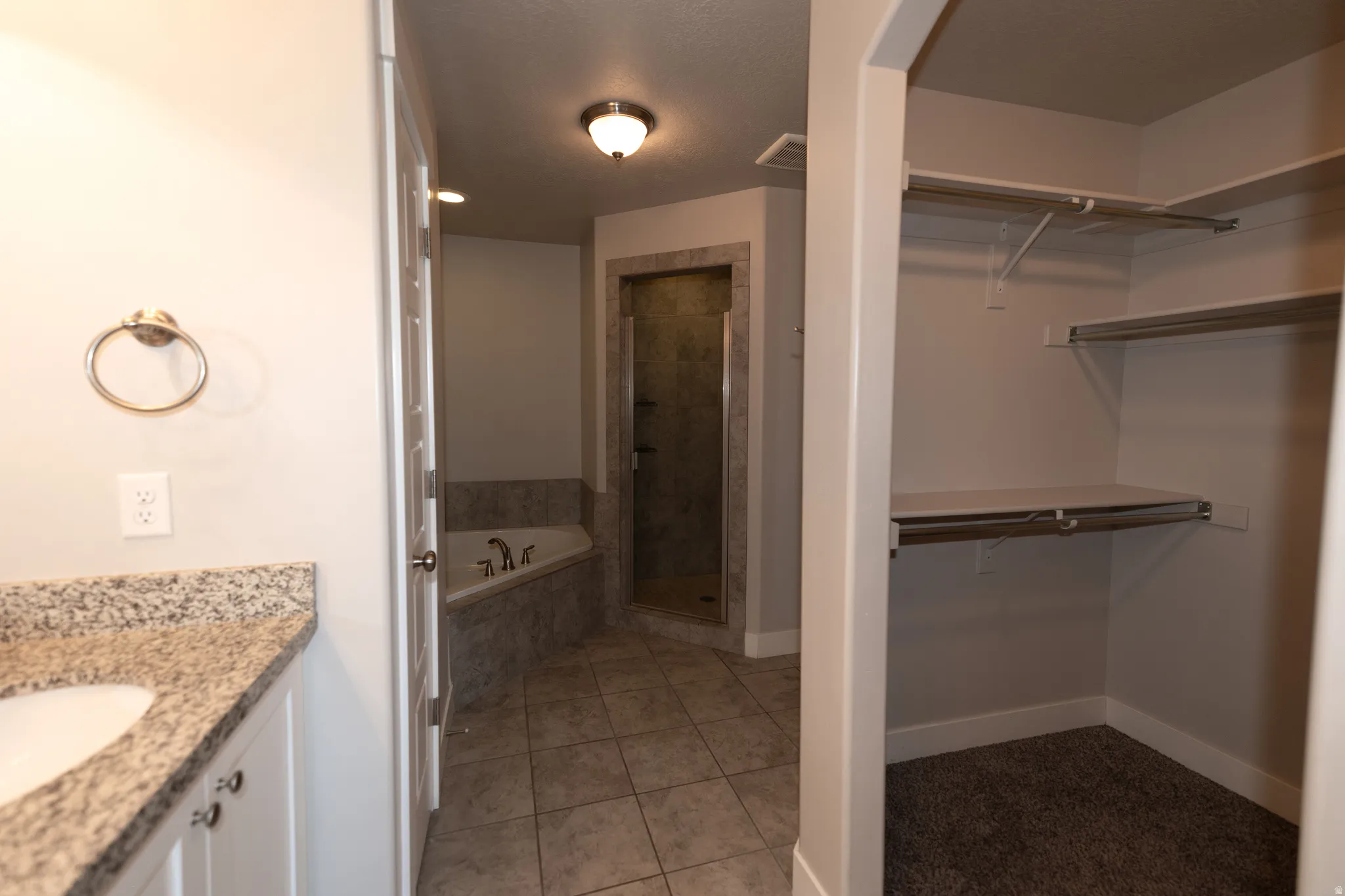 Bathroom featuring a corner soaking tub, a separate glass-enclosed shower, a vanity with a granite-style countertop, and a walk-in closet with shelving and hanging rods