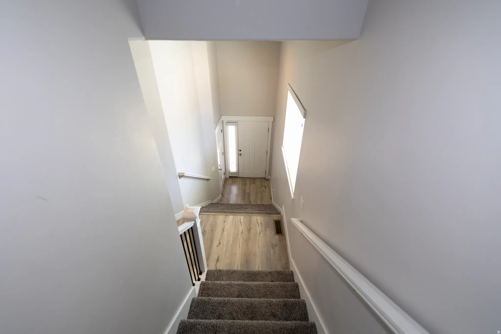 Staircase featuring carpeted treads, white handrail, and dark wood balusters