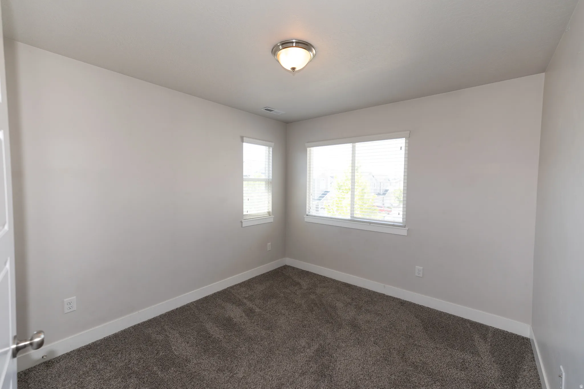Room featuring two windows with white blinds, neutral wall paint, and gray carpet flooring