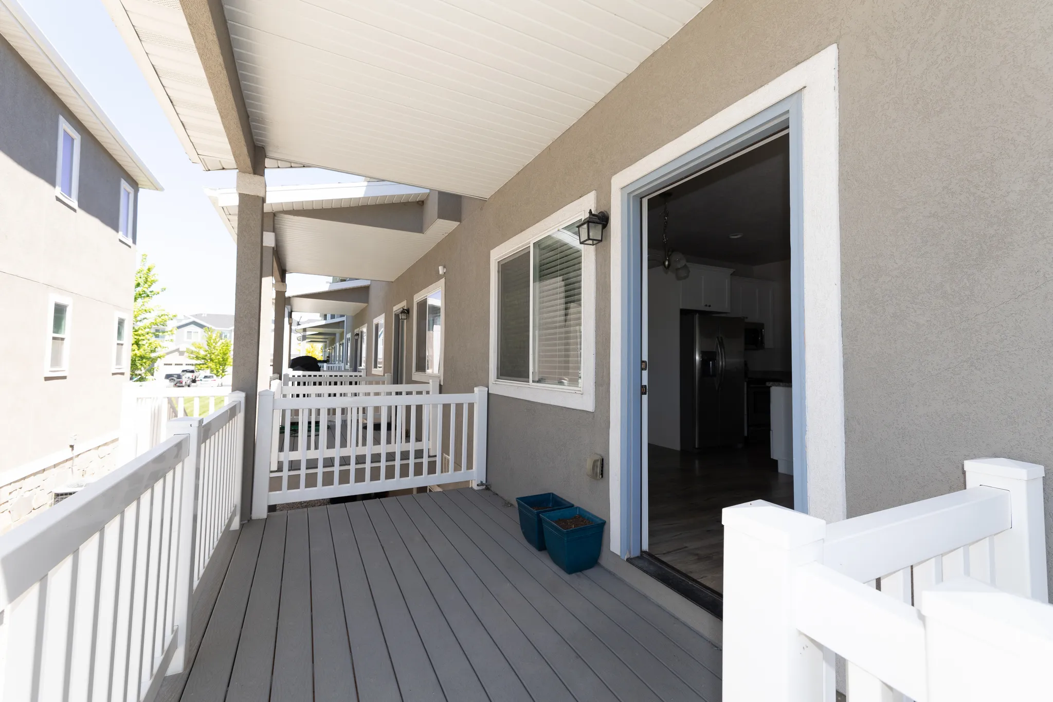 Covered outdoor deck featuring composite decking, white railing, stucco exterior, and sliding glass door access to the interior