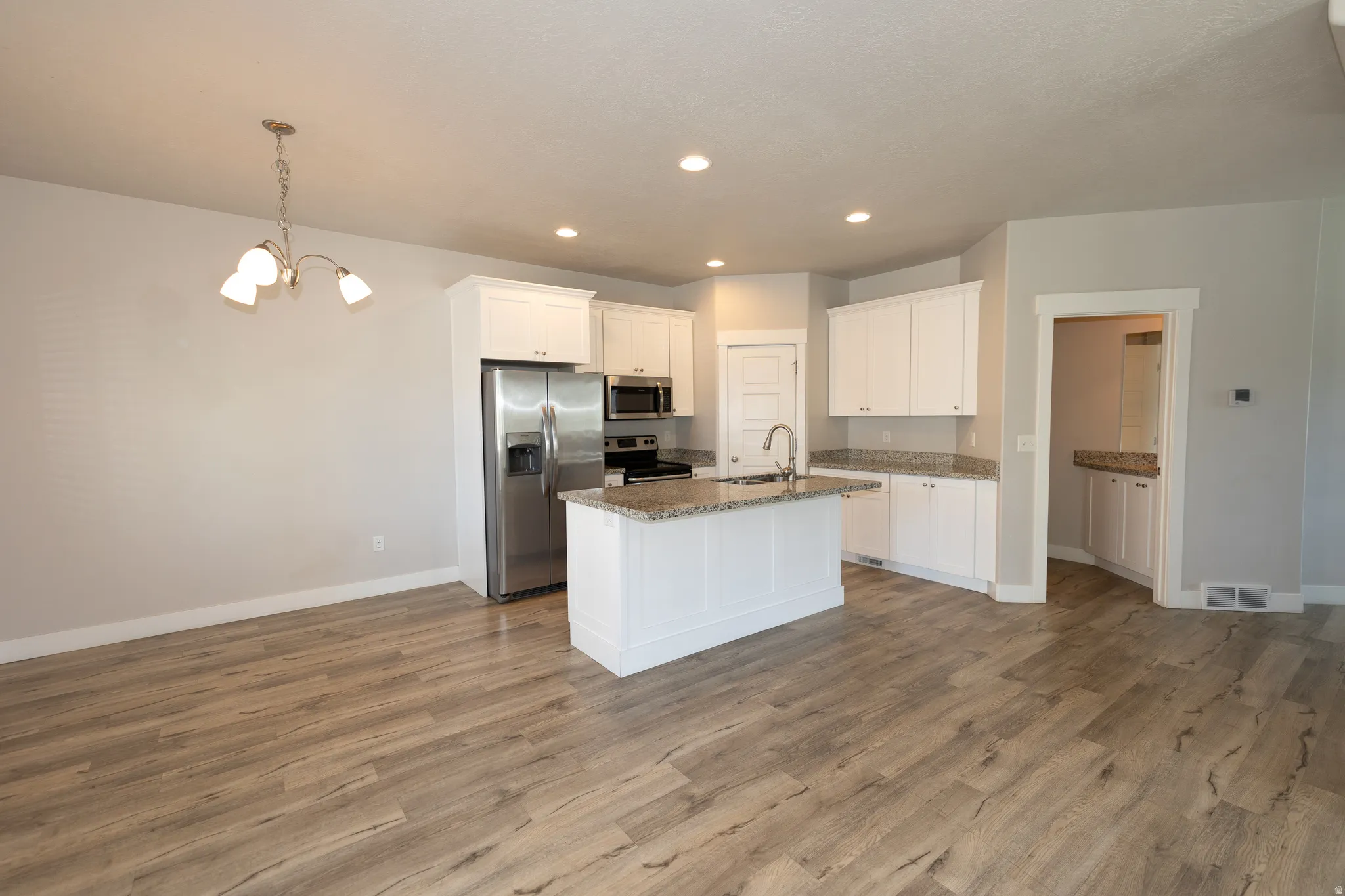 Kitchen and dining area featuring wood-finish flooring, white cabinetry, a center island with a sink, stainless steel appliances, and recessed lighting