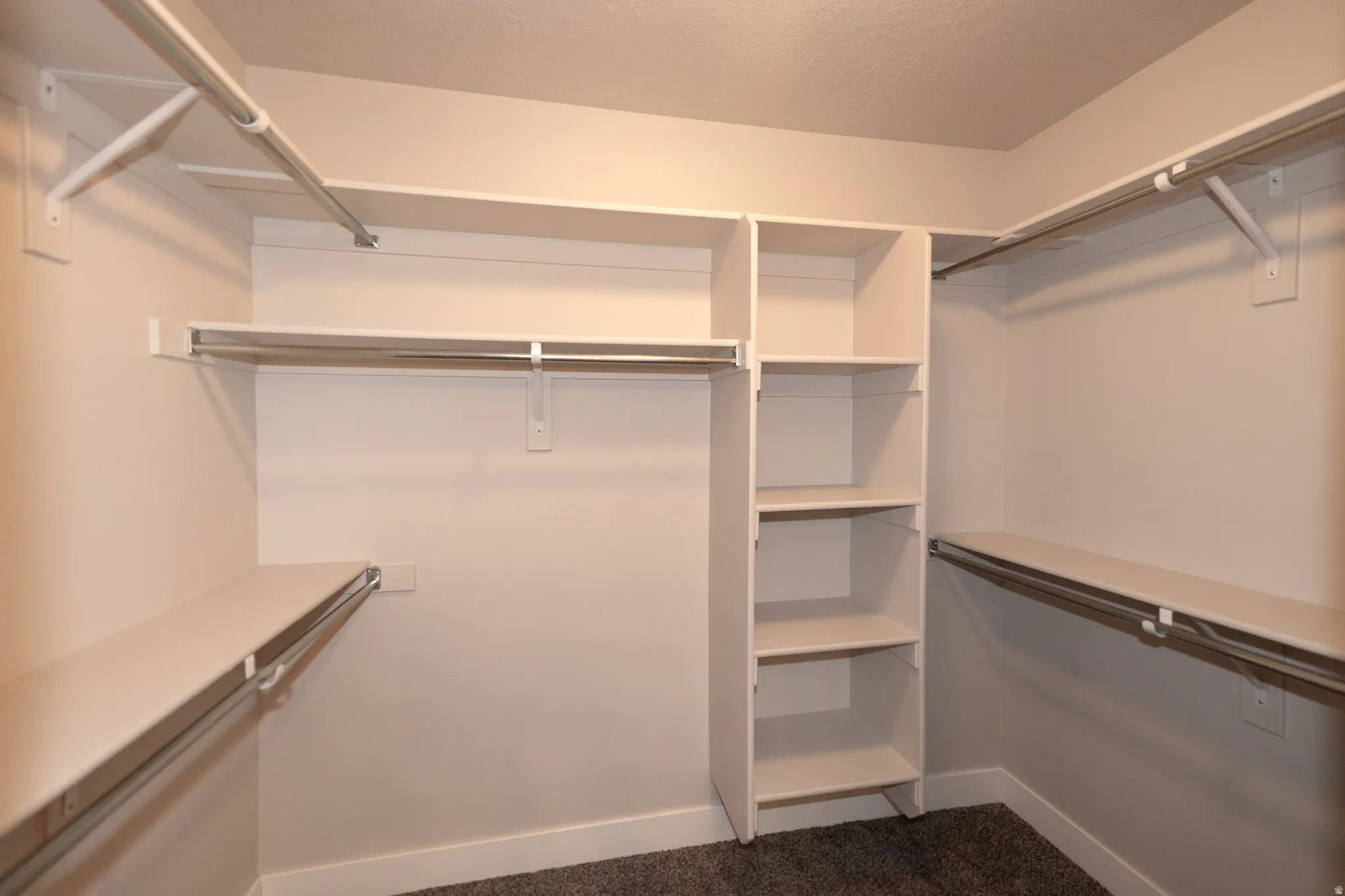 Walk-in closet featuring built-in shelving, multiple hanging rods, and dark carpeting