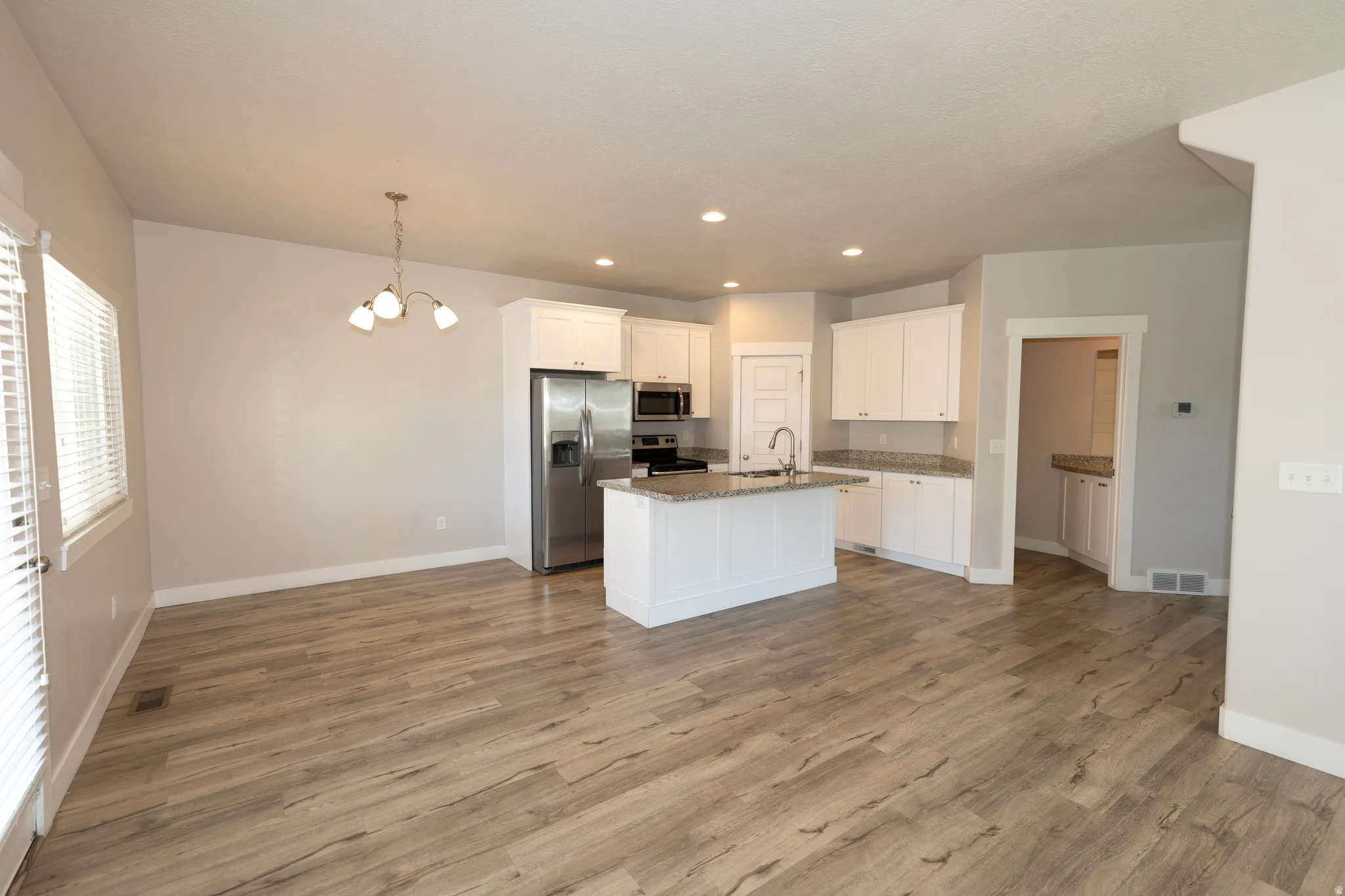 Open concept living area featuring light wood-finish flooring, white cabinetry, a kitchen island with a double basin sink, and stainless steel appliances