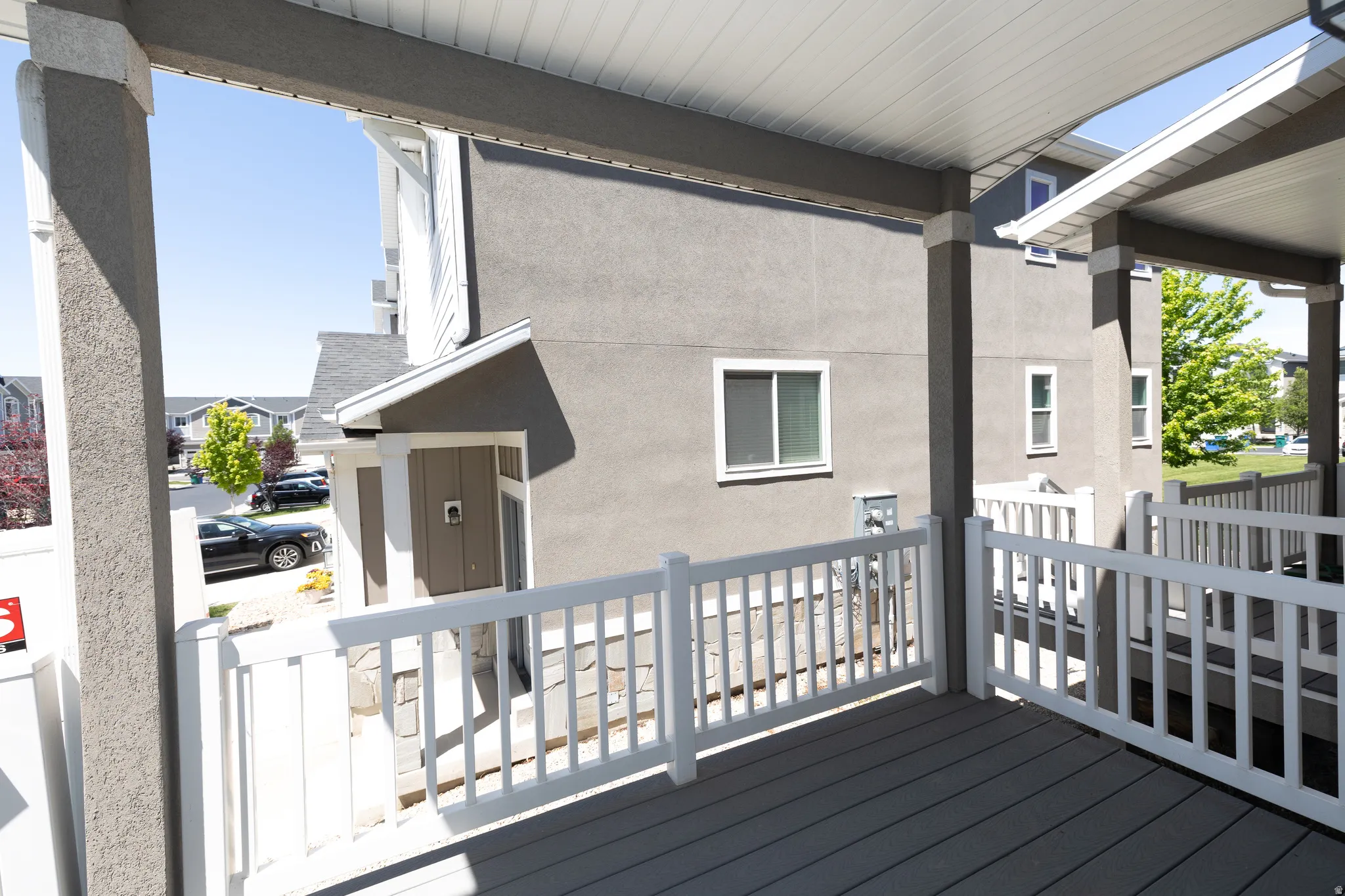 Covered porch featuring white railing, gray composite decking, and gray stucco exterior