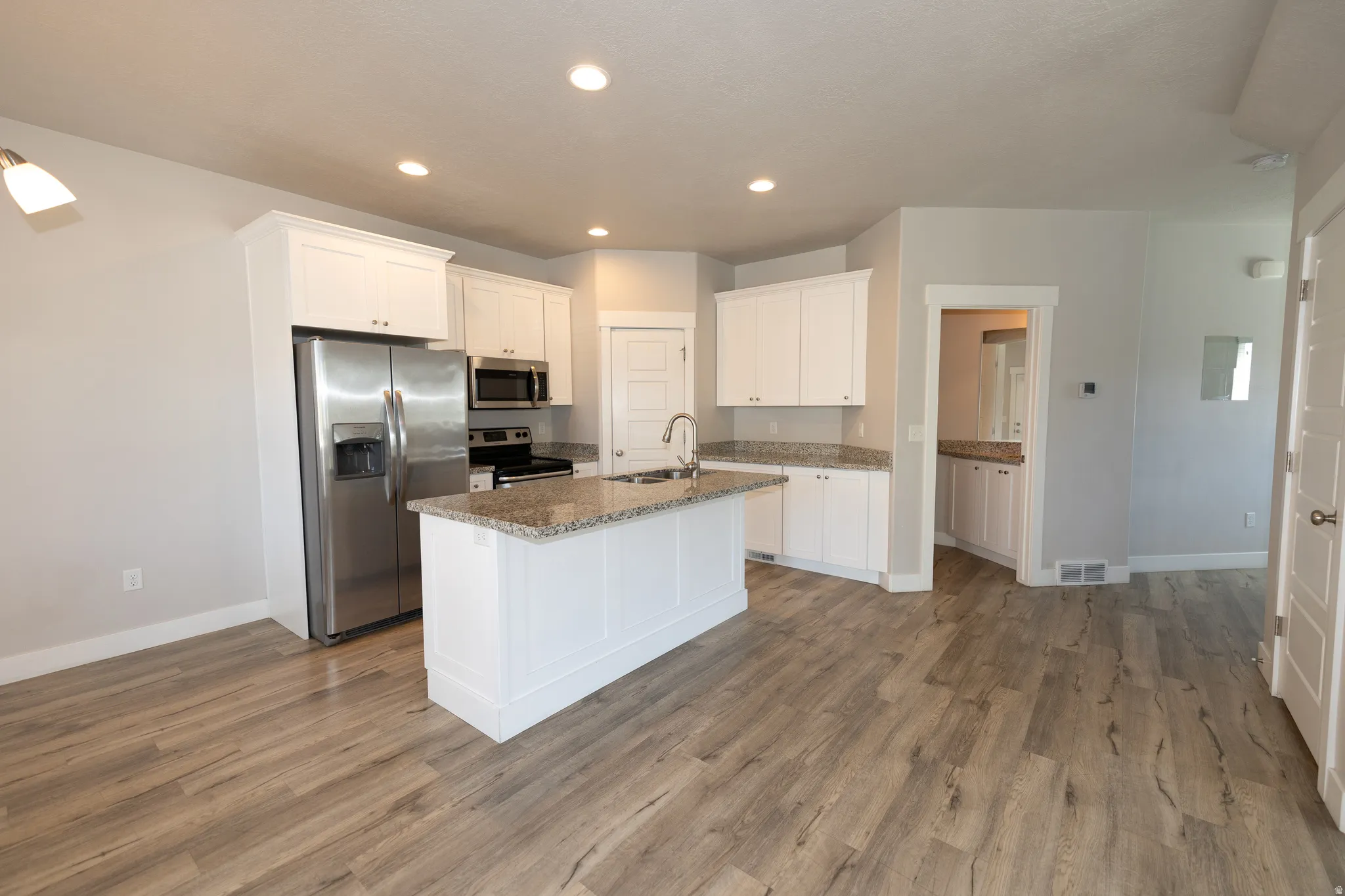 Modern kitchen featuring white cabinetry, stainless steel appliances, a center island with sink, granite countertops, and wood-finish flooring